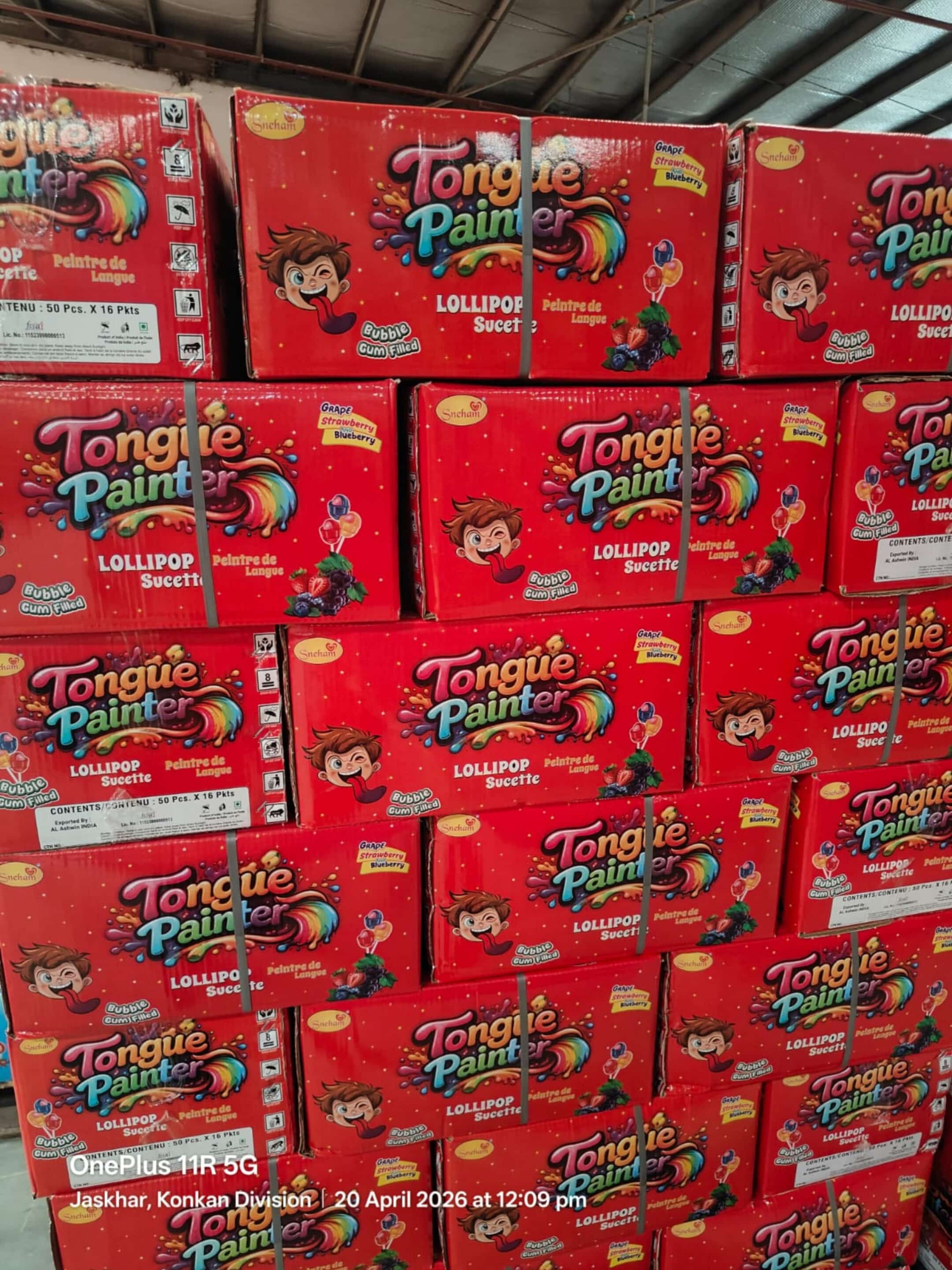 Red glossy toy-box packaging stacked on pallets, labeled 'Tongue Painter' with colorful splash graphics and a cartoon child image on each box (lollipop flavor).